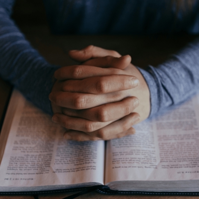 Hands closed in praer over an open bible